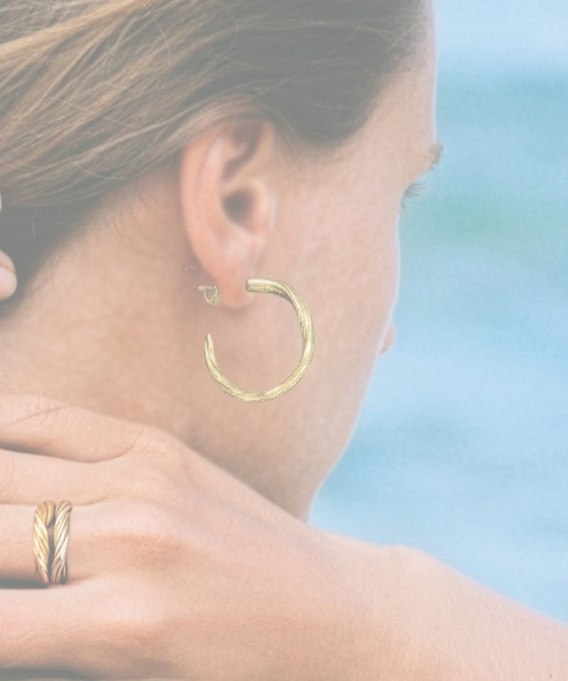 Woman looking at the ocean wearing one-of-a-kind sculptural Pahoehoe earrings hand crafted in 14k gold by Michelle Hoting, jewelry artist