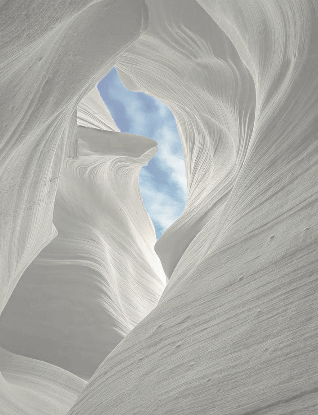 Wind swept sandstone canyon with a cloudy blue sky peeking  through the center canyon ceiling.