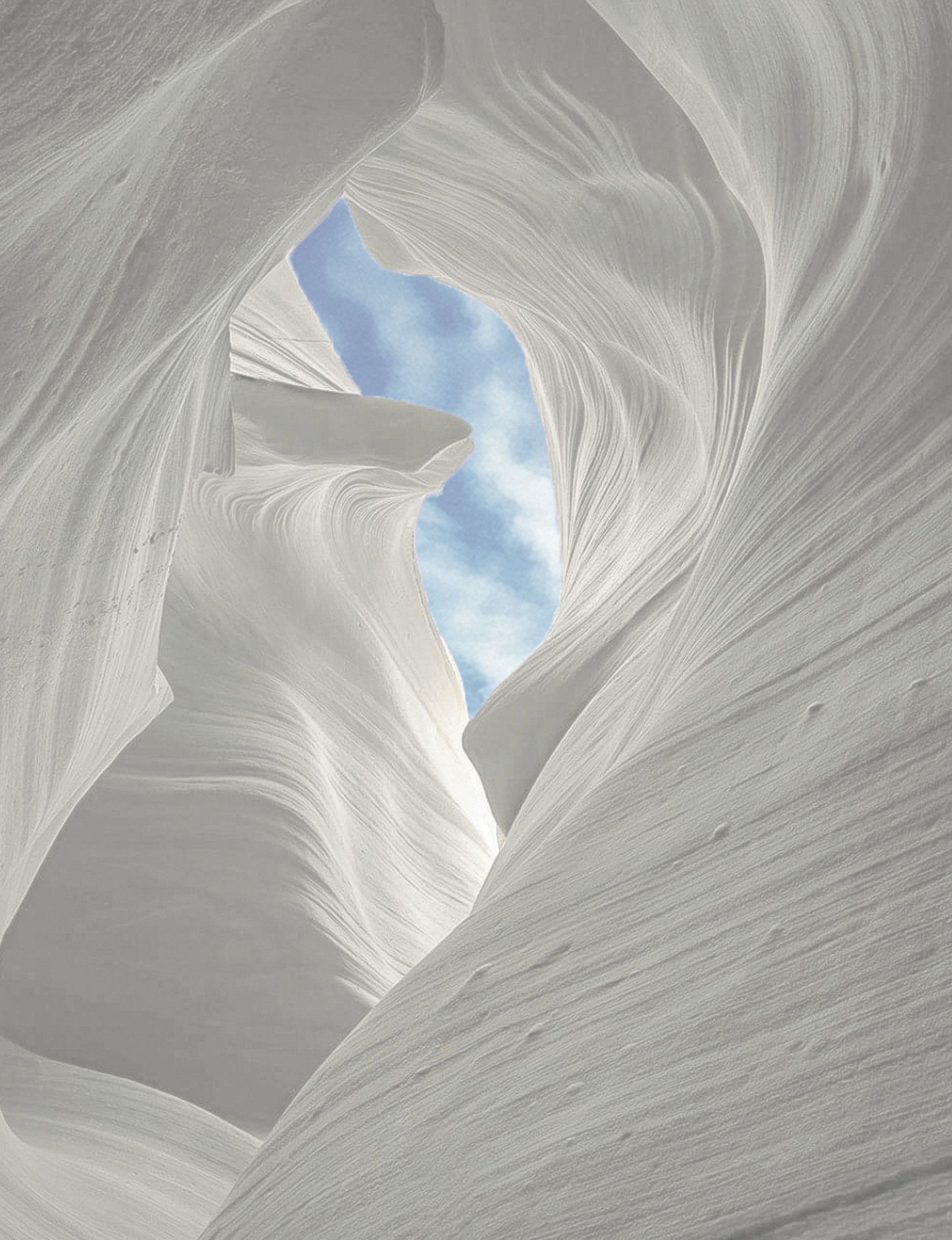 Wind swept sandstone canyon with a cloudy blue sky peeking  through the center canyon ceiling.