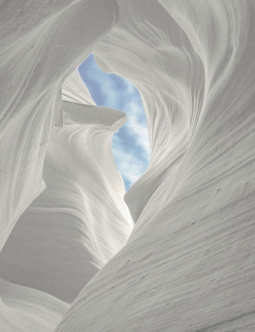 Wind swept sandstone canyon with a cloudy blue sky peeking  through the center canyon ceiling.
