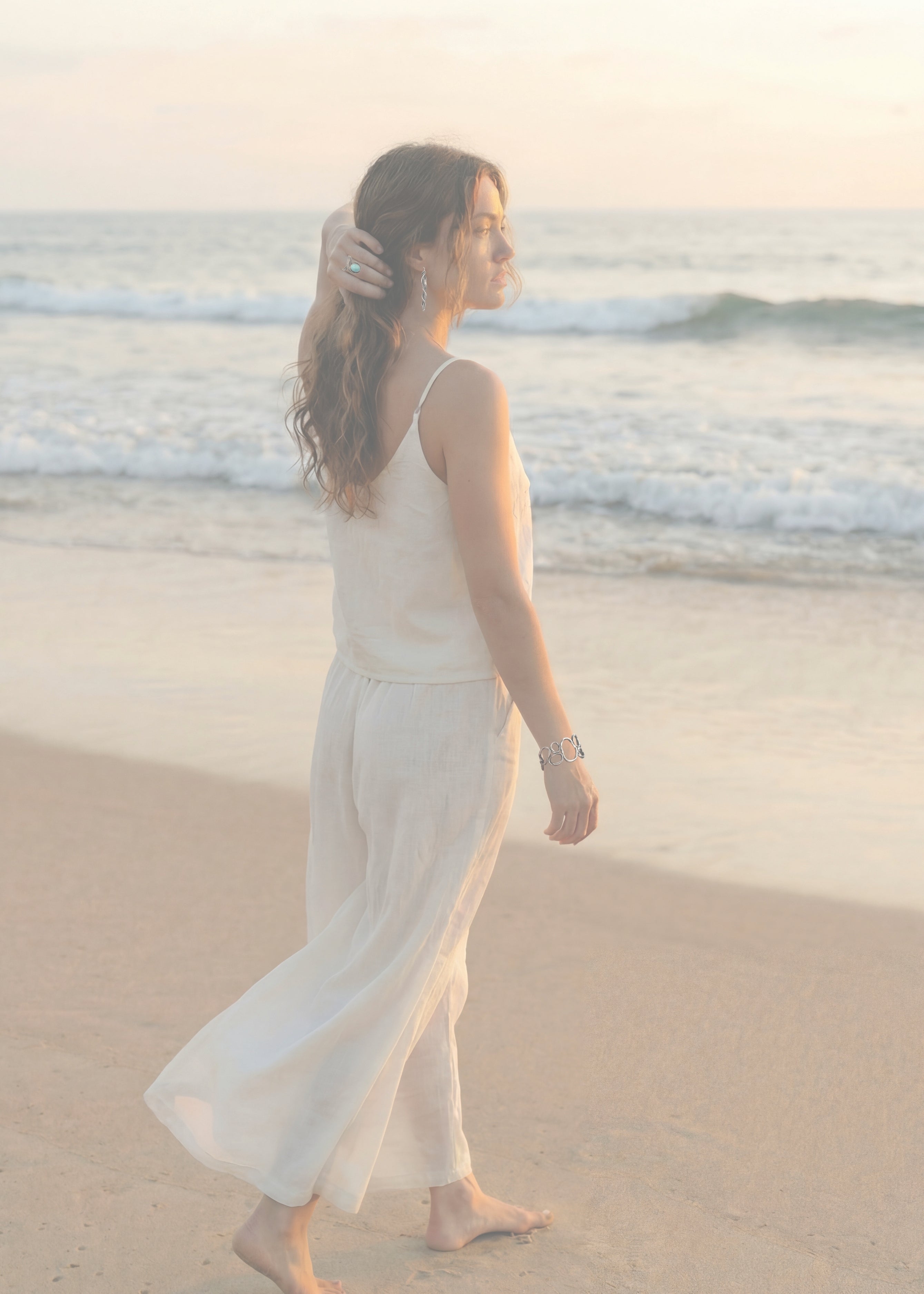 A woman on the beach wearing mitsuro hikime jewelry by jewelry sculptor Michelle Hoting. Beach Pebble Bracelet, Turquoise Cove Ring and Wave Fold Earrings in Sterling Silver