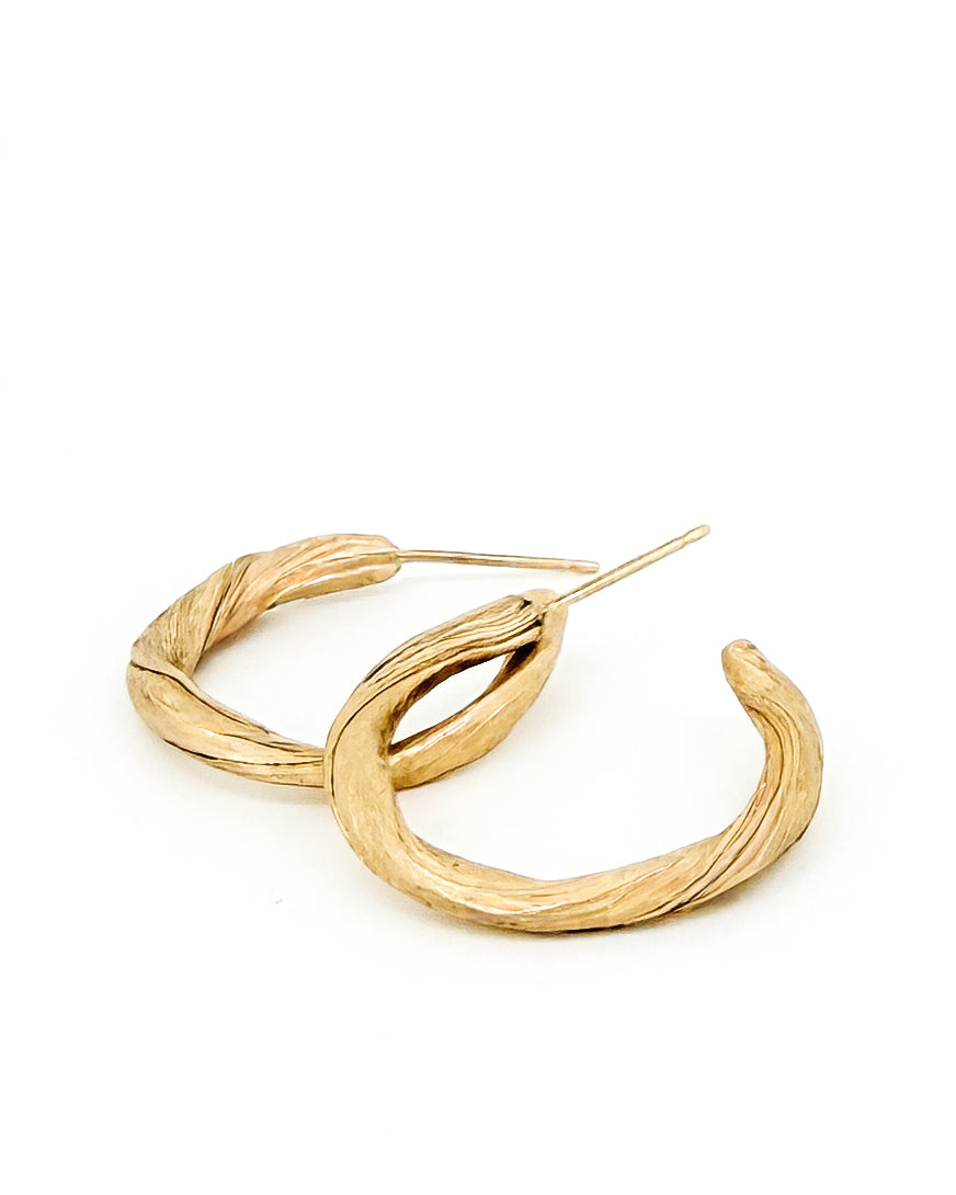 a pair of 14k gold hoop earrings that have a graceful twisting pattern created to resemble pahoehoe lava by jewelry sculptor michelle hoting using mitsuro hikime