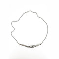 a silver necklace with a sculptural wave like twisting pattern.