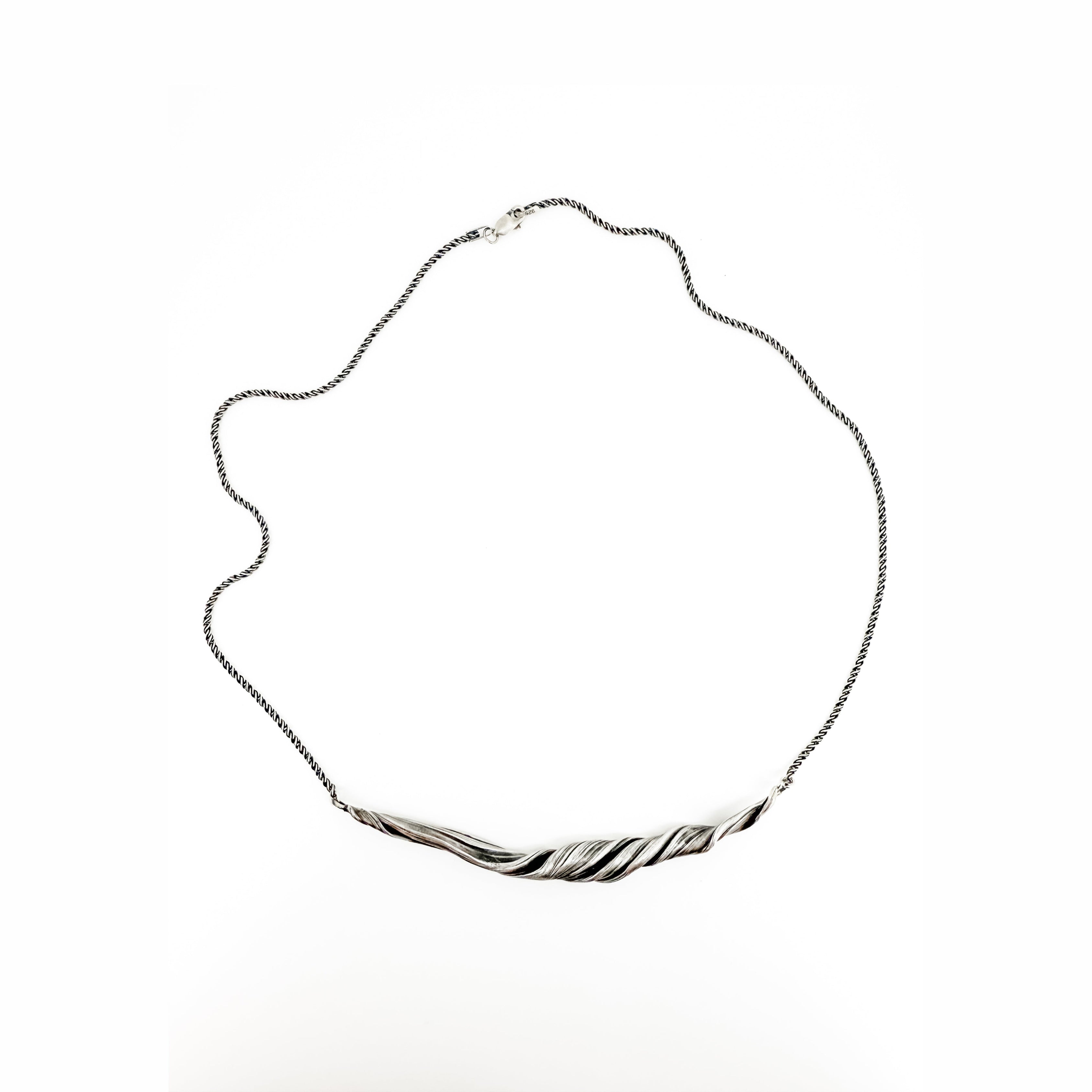 a silver necklace with a sculptural wave like twisting pattern.