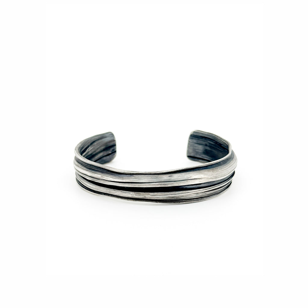 a silver cuff bracelet with a sculptural strata like  pattern.