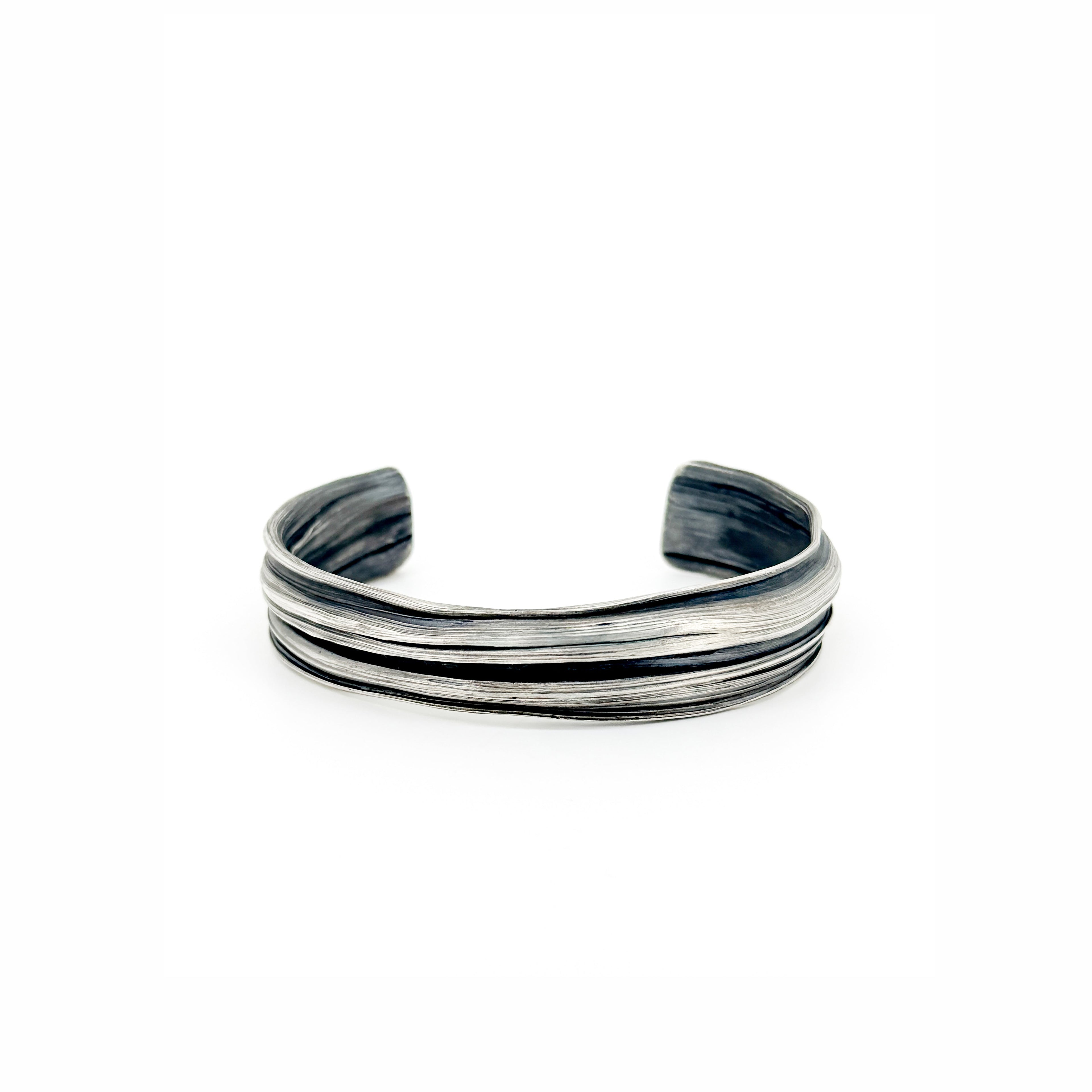 a silver cuff bracelet with a sculptural strata like  pattern.