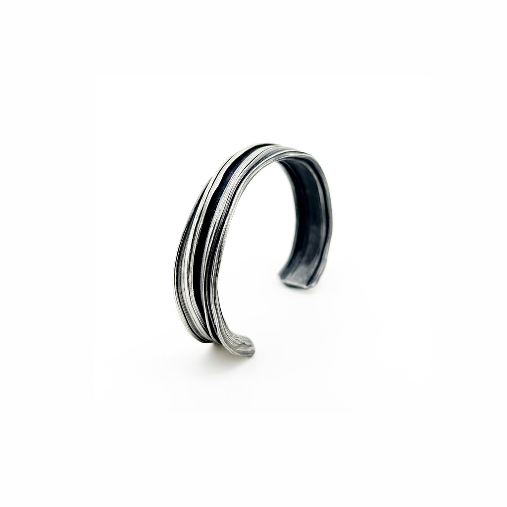 side view of a silver cuff bracelet with a sculptural strata like  pattern hand fabricated by jewelry artist Michelle Hoting using the Mitsuro Hikime technique