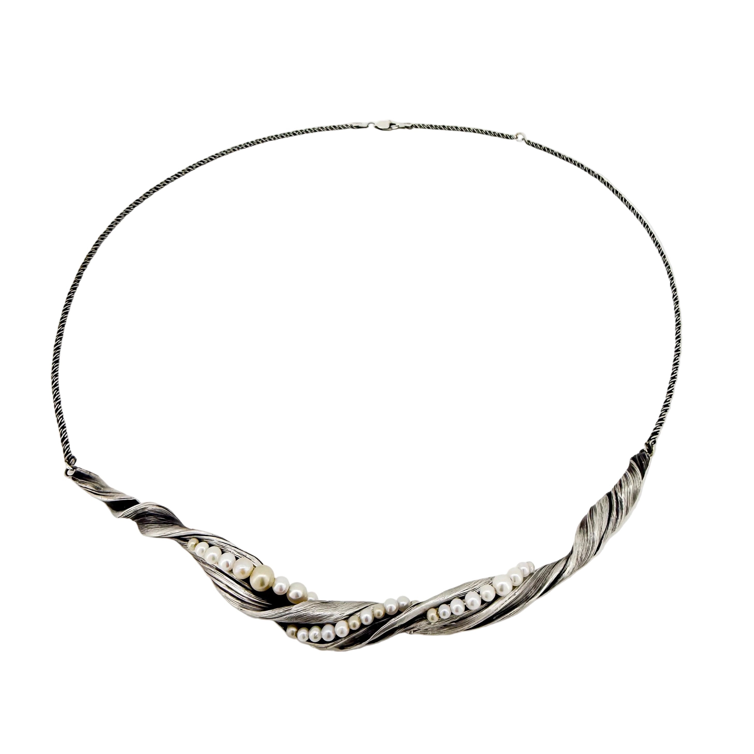 a twisting silver necklace with pearls that look like sea foam  along the edge of waves washing up on the shore