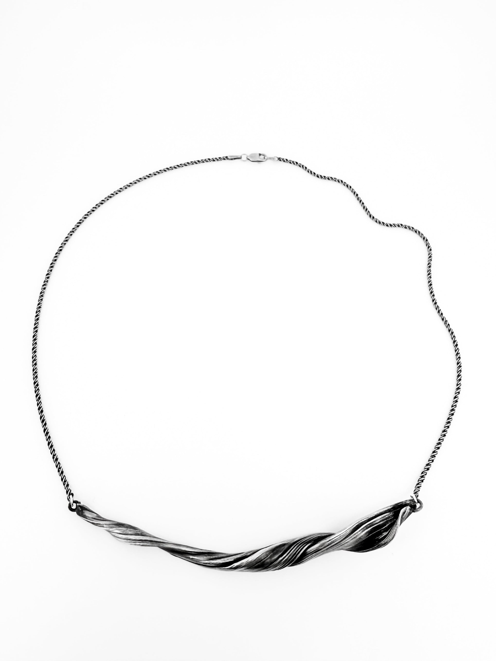 a sterling silver necklace with a sculptural wave like twisting pattern.