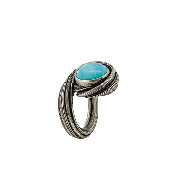 A sculptural sterling silver ring set with a vivid turquoise cabochon. The silver band flows upward in layered curves that cradle the stone, creating a sense of movement similar to water circling within a quiet coastal cove by Michelle Hoting